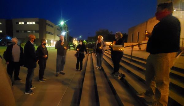 Adults stand on and around the steps of Racine's city hall at night, holding candles for NAMI's Mental Illness Awareness Week Candlelight Vigil.
