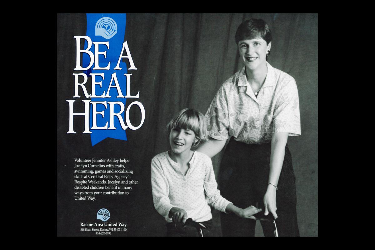 A poster from United Way's days as Racine Area United Way. The background is a black and white photo of a young adult with dark, buzzed hair, lipstick and earrings putting their hand on the back of a child beside them, who has a blonde bowl cut and stands with a walker. Both are smiling. Beside them, a blue ribbon with an early version of the United Way logo drops down and says, 