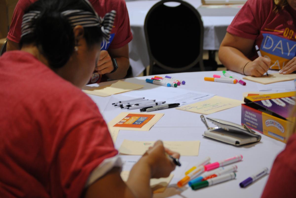 Photo of Day of Caring volunteers around a table, filling in coloring pages for kids.