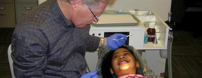 A kid reclining in a dentist chair grins up at one of Health Care Network's volunteer dentists.