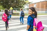 A girl smiles at the camera as she walks into a crosswalk