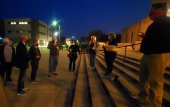 Adults stand on and around the steps of Racine's city hall at night, holding candles for NAMI's Mental Illness Awareness Week Candlelight Vigil.