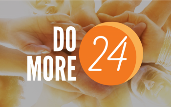 Do More 24 logo over a glowing photo looking up on a group of people holding hands.